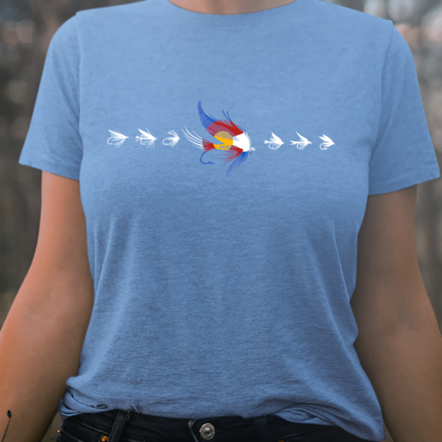 Women's fly fishing t shirt.  Colorado blue colored women's tee.  The Fly CO Tee by Headwater Canyon.  Fly fishing shirt depicts a number of fishing flies with the Colorado flag colors on a woman model.