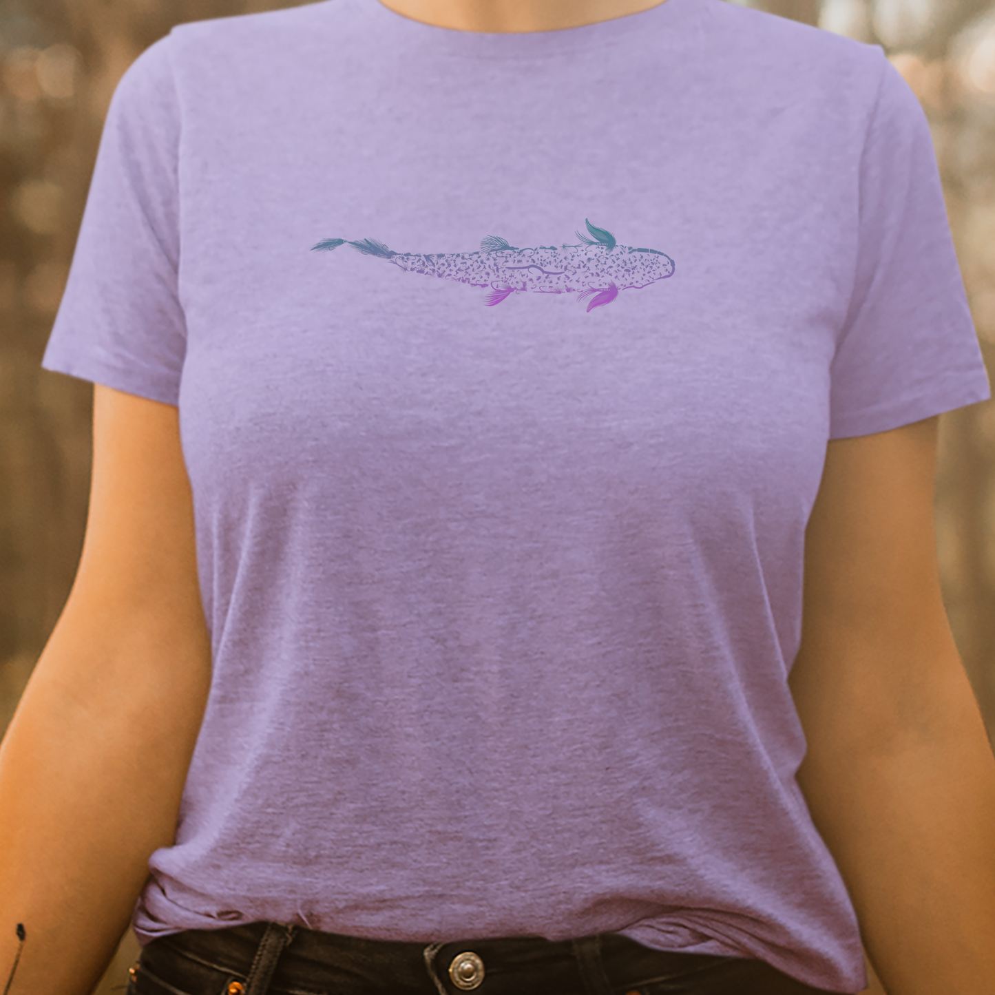 Women's fly fishing t shirt on a woman.  Lavender colored women's tee.  Trout is Fly Tee by Headwater Canyon.  Fishing flies form a trout.