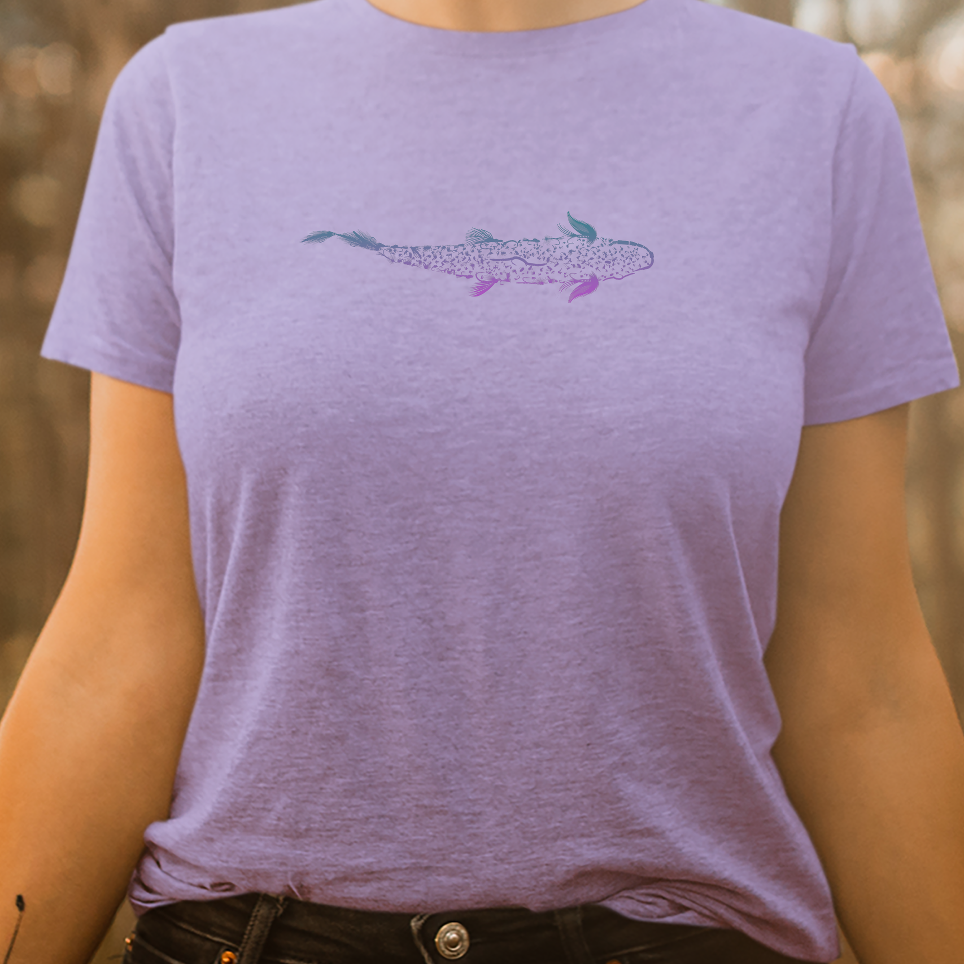 Women's fly fishing t shirt on a woman.  Lavender colored women's tee.  Trout is Fly Tee by Headwater Canyon.  Fishing flies form a trout.