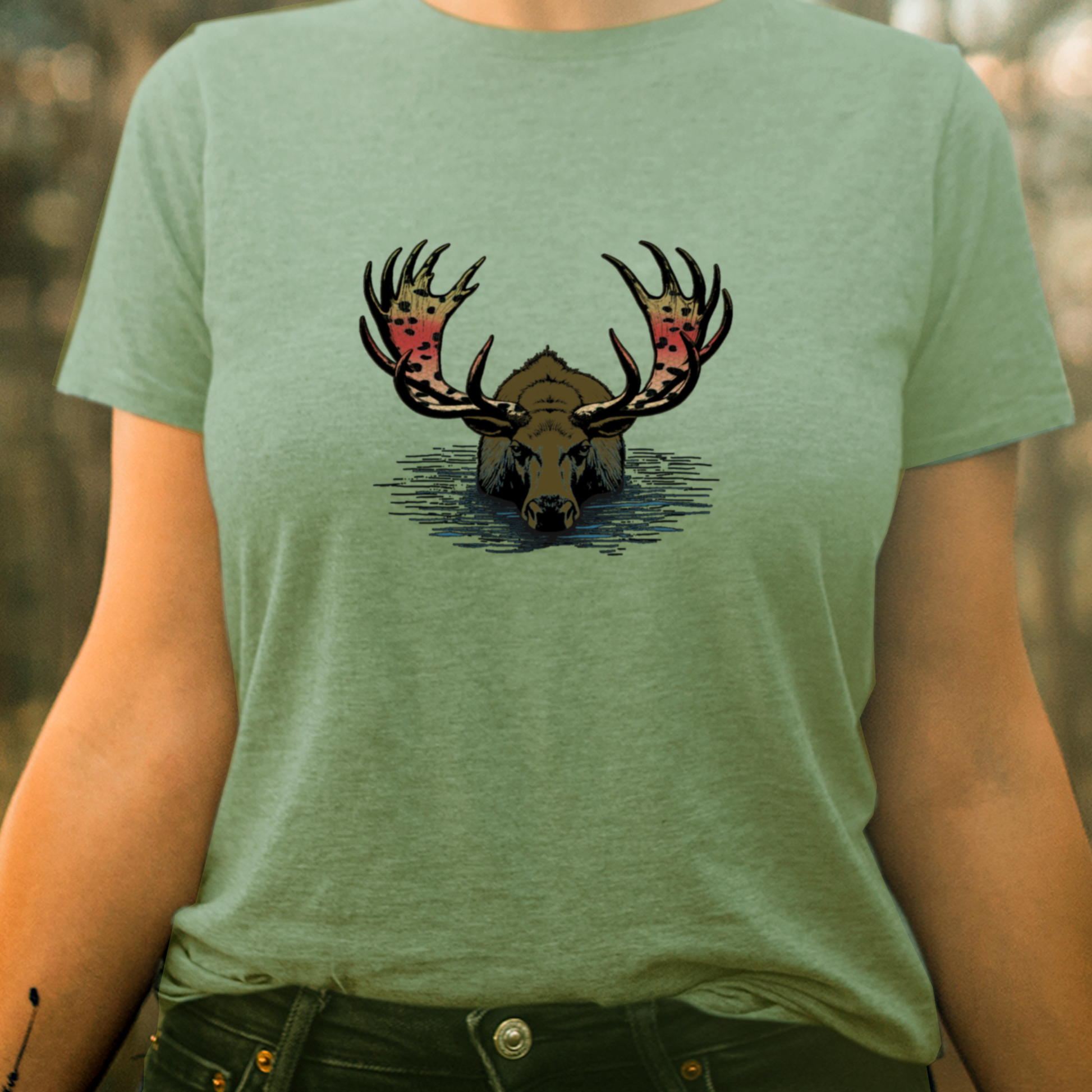 Women's fly fishing t shirt.  Sage colored women's tee.  Rainbull Tee by Headwater Canyon.  Fly fishing shirt depicts a moose in the water with a rainbow trout pattern on his horns on a woman.