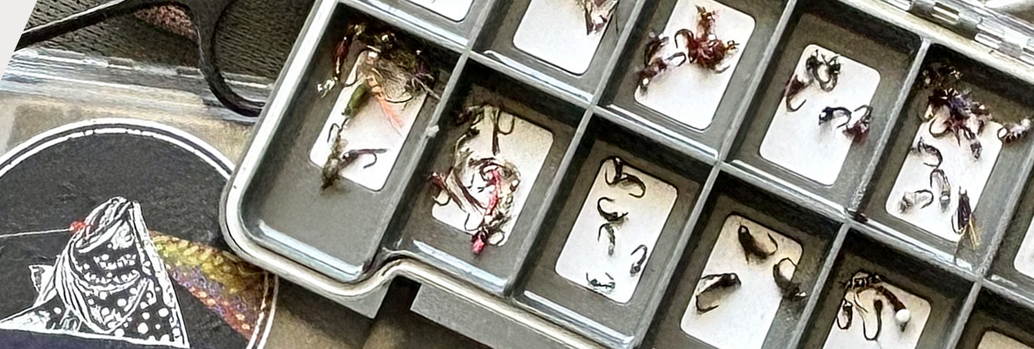 Picture of multiple fly fishing boxes with one box open displaying multiple hand tied fishing flies.